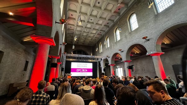 Picture of a stage showing a screen reading EPC2024. Conference attendees sit in chairs in front of the stage.